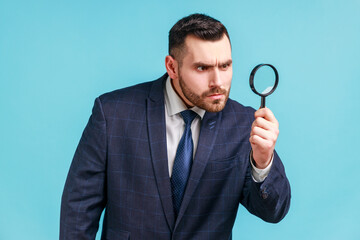 Serious man with beard wearing in dark suit looking away through magnifying glass, spying, finding...