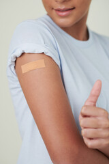 Close-up of teenage girl with plaster on her shoulder showing thumb up after vaccination at hospital