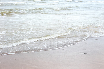 Small seaside waves near shoreline in sand.