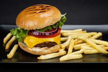 Tasty homemade beef burger with fresh ingredients and french fries served in a black plate, close-up view.