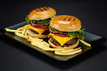 Pair of delicious homemade beef burgers with french fries in a black plate, close up view