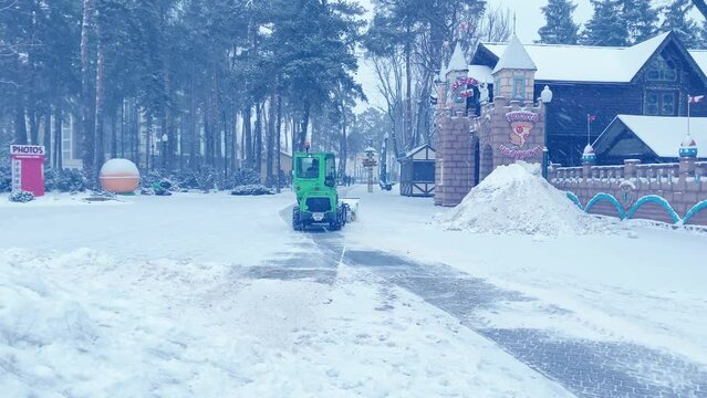 Snowplow Tractor works on snow removal in the park during snowfall on Christmas day. Tractor cleans the path of the park from snow: January 2022 - Kharkiv, Ukraine