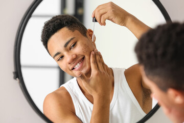 Young African-American guy using serum for skin care in bathroom