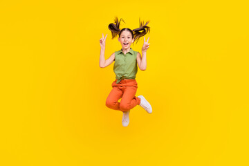 Fototapeta na wymiar Photo of cute charming preteen girl dressed green top showing two v-signs jumping high smiling isolated yellow color background