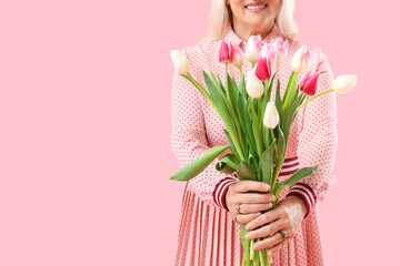 Smiling mature woman holding bouquet of tulips on pink background, closeup. International Women's...
