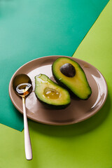 Two slices of avocado on pink plate with a spoon on green abstract geometric background, copy space