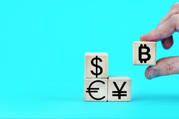 Wooden cubes with currency signs, icons. Hand adding bitcoin symbol