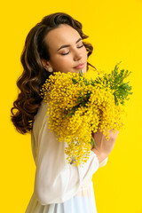 Beautiful young woman with mimosa flowers on yellow background