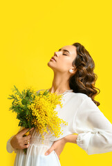 Beautiful young woman with mimosa flowers on yellow background