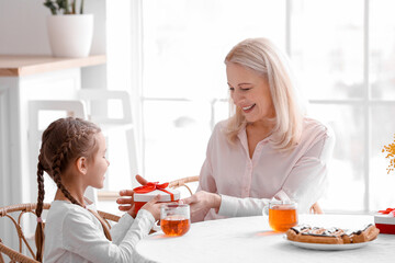 Obraz na płótnie Canvas Little girl greeting her grandmother with gift in kitchen on International Women's Day