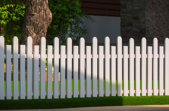 Front view of white wooden fence on artificial turf with sunlight and shadow on surface in front yard area at home