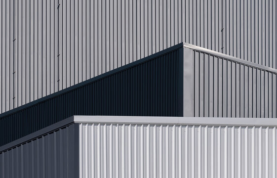 Sunlight and shadow on surface of gray and white corrugated metal industrial buildings in low angle view 