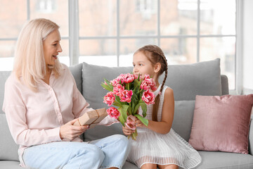 Little girl greeting her grandmother with tulips at home on International Women's Day