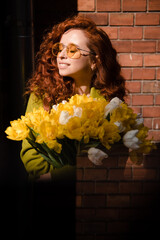 Stylish woman with red curly hair with a bouquet of yellow tulips