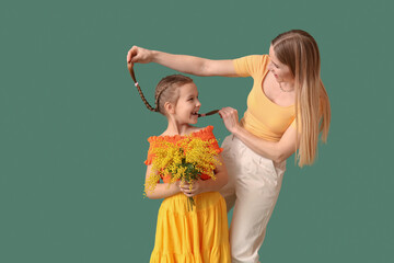 Little girl with mimosa flowers and mother on green background