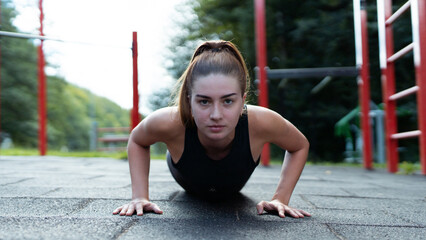Beautiful Young Red Haired Caucasian Woman Working Out in an Outside Environment. Girl Stretching in an Outdoor Gym Surrounded by Red Metal Bars.
