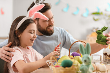Fototapeta premium Cute little girl with her father painting Easter egg in kitchen