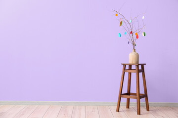 Vase with tree branches and Easter decor on stool near color wall in room