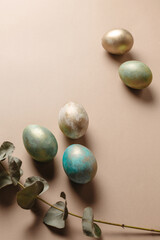 Creative eggs with eucalyptus on a brown background. Beautiful postcard for Easter day. Stylishly decorated eggs with gold