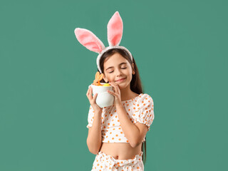 Cute little girl with bunny ears, toy rabbit and Easter eggs on green background
