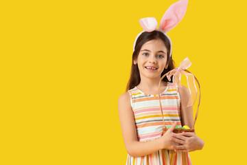 Cute little girl with bunny ears and Easter basket on yellow background