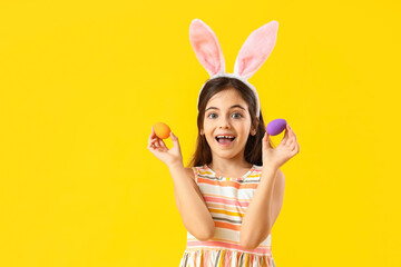 Happy little girl with bunny ears and Easter eggs on yellow background