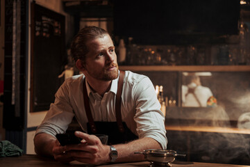Caucasian male bartender sitting alone at bar texting on cellular device 