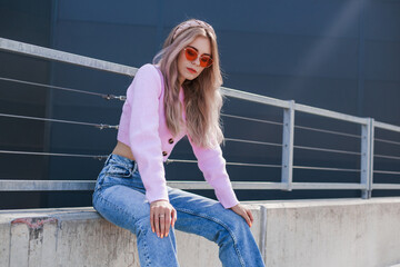 city walk in a modern form. Beautiful girl in a pink sweater and jeans and pink glasses. Modern style, positive attitude, urban look