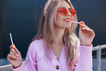 Lady chewing gum on the background of the shopping center. Beautiful girl in a pink sweater and jeans and pink glasses. Modern style, positive attitude, urban look
