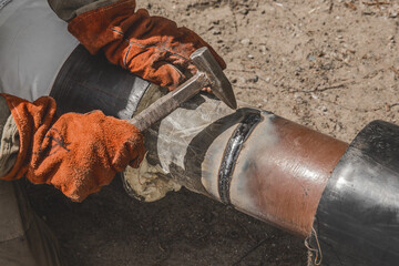 Welder with a hammer in hand and working mittens removes slag after welding industry work the...