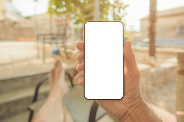 Man sitting on apartment terrace with feet on the table looking at mobile smart phone mockup screen
