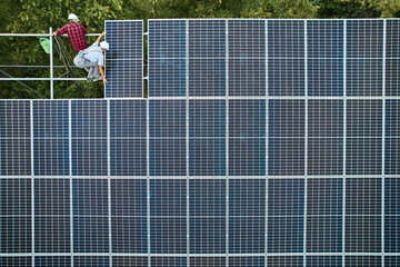Aerial view of men technicians installing photovoltaic solar panels to high steel platform. Concept...