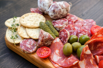 Various types of salami on a wooden board, served with olives, crackers and pickles and cracker. Food for an aperitif and dinner lunch in the restaurant. 