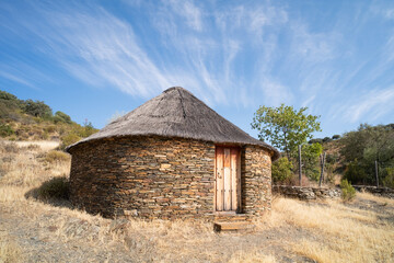 Fototapeta na wymiar Old cabin or hut with a round shape and slate stone walls and a broom and straw roof