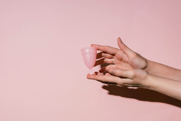 Pink menstrual cup in female hands. Women's health, hygiene concept. Shadow of a hand on a pink wall.
