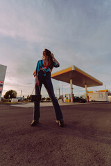 Chica delgada de pelo ondulado poniéndose botas y tomándose fotos en gasolinera