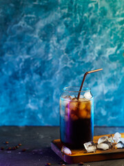 A glass of cold brew coffee on the table, an icy summer drink. Blue background with copy space