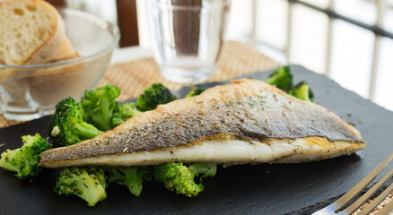 fried fillet of sea bass with garnish of broccoli on black warm stone plate