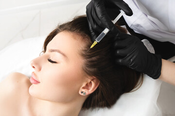 Mesotherapy,  vitamin injections in head skin of hair area. Professional hair loss treatment. Close up view of woman head and doctor's hands with syringe.