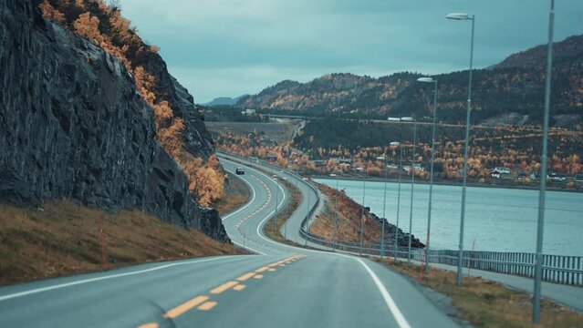 Two-lane road following the Alta fjord coastline. The town of Alta is in the background.