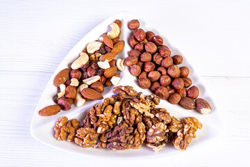 Various nuts close-up on a white plate on a white wooden table.