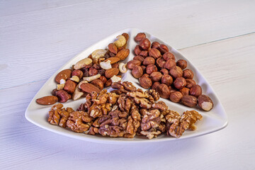 Various nuts close-up on a white plate on a white wooden table.