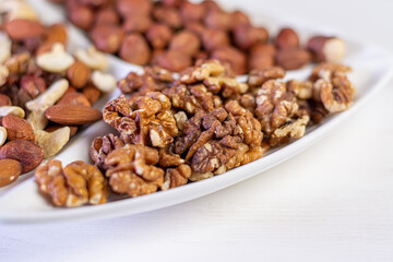 Various nuts close-up on a white plate on a white wooden table.