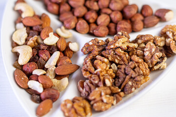 Various nuts close-up on a white plate on a white wooden table.