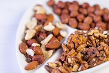 Various nuts close-up on a white plate on a white wooden table.