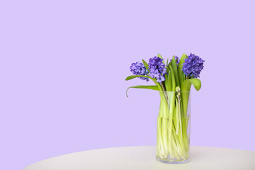 Vase with hyacinth flowers on table against color wall