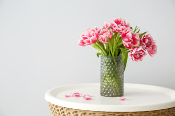 Vase with tulips on table near light wall