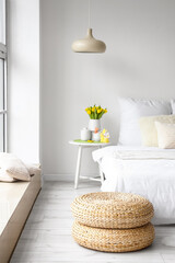 Vase with tulips, cups and Easter rabbits on table near light wall in bedroom interior