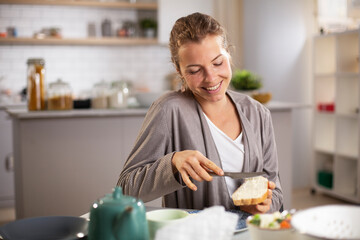 Beautiful woman enjoying in breakfast. Happy young woman eating sandwich at home.