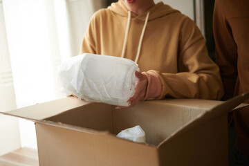 Close-up of woman unpacking the cardboard box with kitchen utensil, she getting the parcel